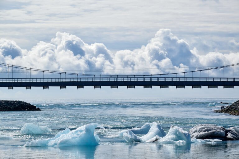 Bridge over water with icebergs, visually aligned so that a cloud seems to sit on top of it.