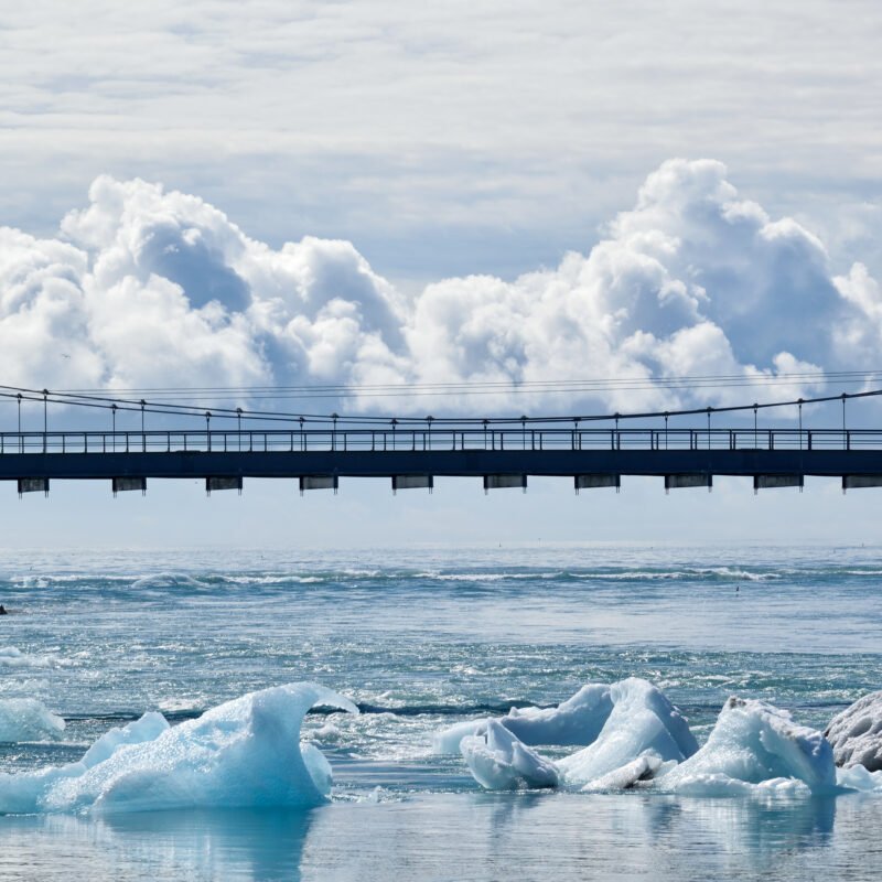 Bridge over water with icebergs, visually aligned so that a cloud seems to sit on top of it.